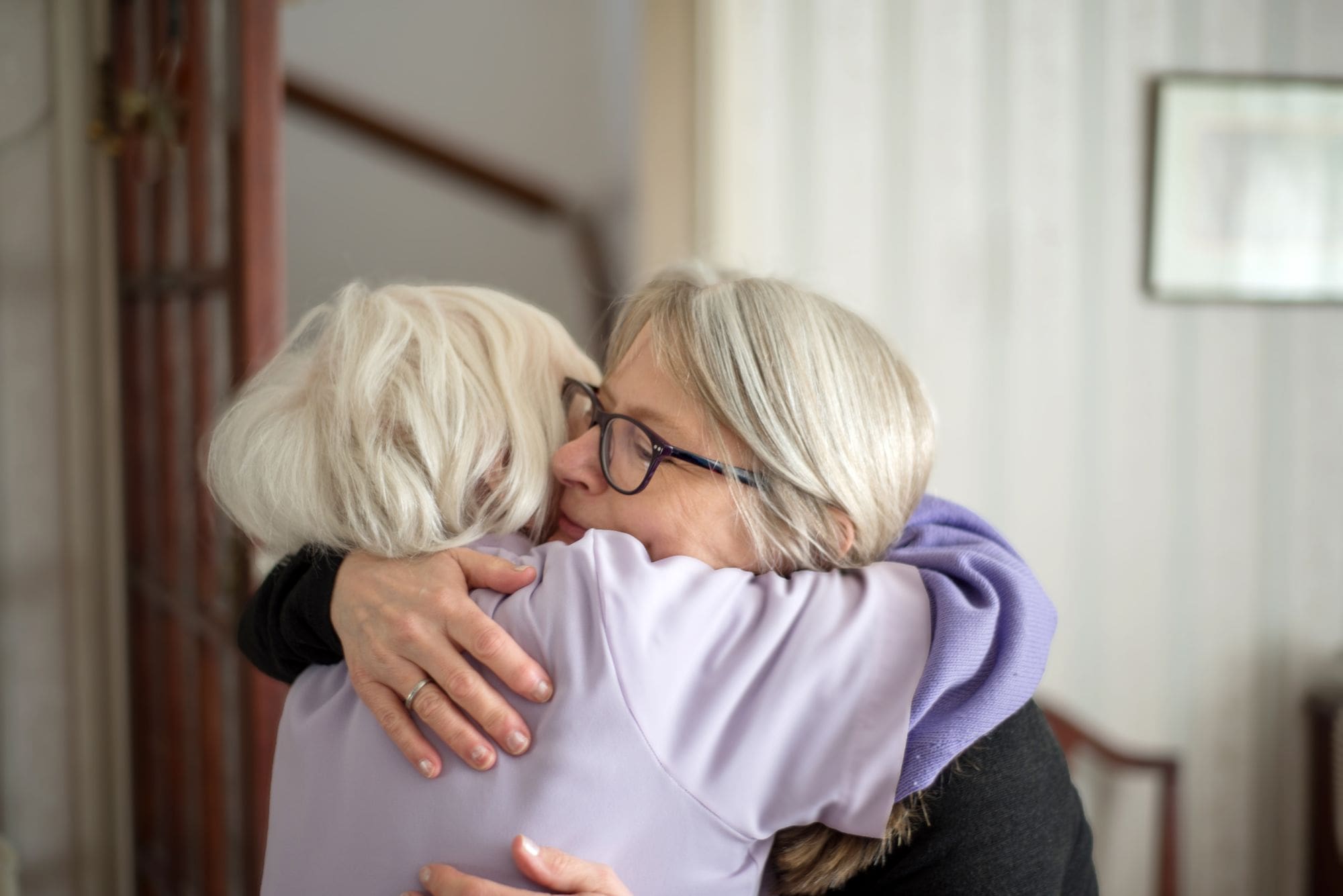 daughter hugging senior mother in living room